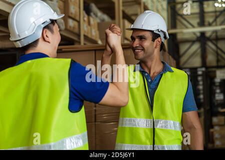 Indian male factory warehouse worker working in logistic industry indoor. Friends greeting and doing handshake with hand grasp inside depot Stock Photo
