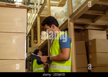 Group of young industrial factory warehouse workers working in logistic industry indoor. Asian and Indian ethnic men man holding a clipboard checking Stock Photo