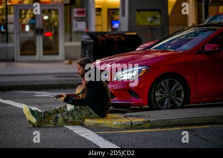 young man sitting in intersection, playing guitar, Vancouver, British Columbia, Canada Stock Photo
