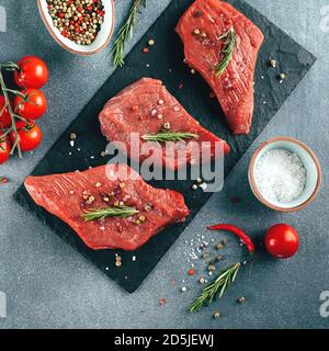 Raw meat. Raw beef steak on a black board with herbs and spices. Top view Stock Photo