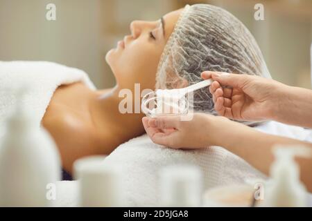 Hands of cosmetologist preparing moisturizing mask for applying on young womans face Stock Photo