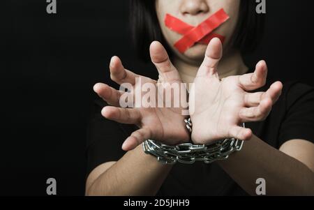 Asian woman blindfold wrapping mouth with red adhesive tape and she was hand tethered interpreter chain black background. Freedom speech censorship an Stock Photo