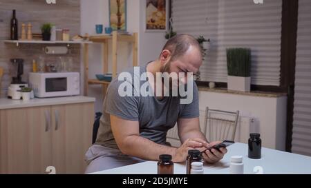 Man with headache using smartphone to search informations. Stressed tired unhappy worried person suffering of migraine, depression, disease and anxiety feeling exhausted with dizziness symptoms. Stock Photo