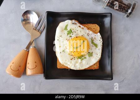 Fried Egg on Whole wheat Toast with salt and pepper for classic Breakfast. sunny side up egg with brown bread on black plate over wooden table. Stock Photo
