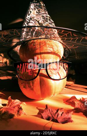 Two Halloween orange pumpkins standing one on top of other in festive bloody glasses and witch hat with spiderweb. Stock Photo