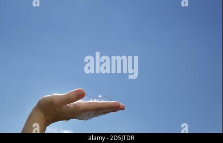 Closeup Female hand palm up with soap bubbles on blue sky background  Stock Photo