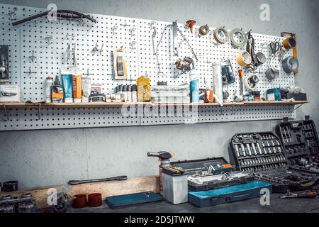 Moto workshop with hand mechanic tools kit. Workbench with sets of keys, screwdrivers, ploskobets, electrical tape, duct tape on wall. Table with moto Stock Photo