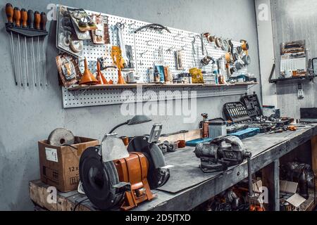 Garage. Workspace moto, auto workshop close-up. Workbench with vise, grinder, sets of keys, equipment, spare parts. Old tools hanging on a steel wall Stock Photo