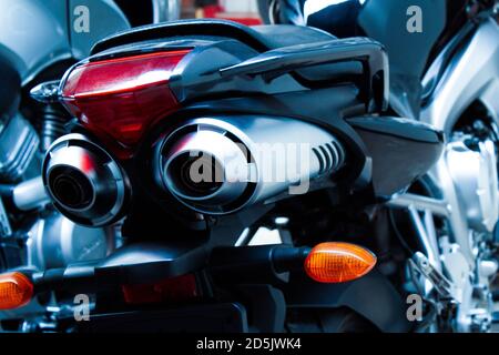 Exhaust pipes and brake light of a motorcycle closeup. The noise of a sports bike in a garage. Rear view of a classic road bike. A pair of chrome pipe Stock Photo