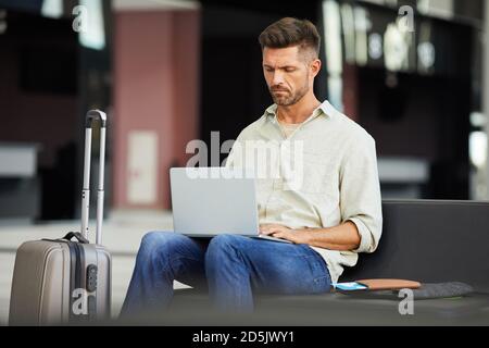 Young businessman working on laptop while sitting in waiting room at the airport Stock Photo