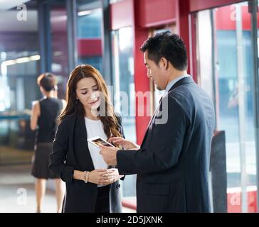 asian business man and woman standing and talking in company elevator hall using digital tablet Stock Photo