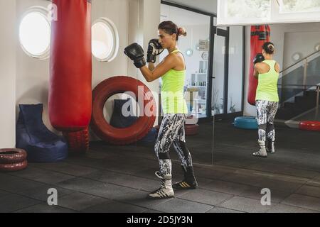 Young female trains in the gym and do boxing exercises in boxing gloves in front of a punching bag Stock Photo