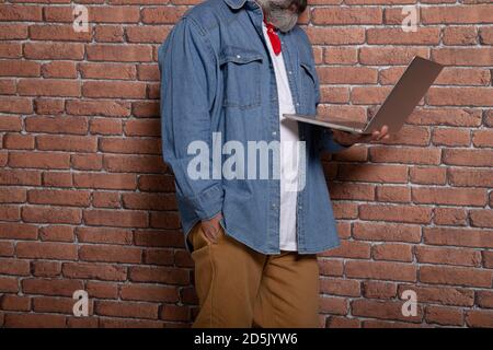Modern man leaning on the brick wall holds a laptop. Coworking space Stock Photo