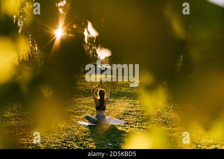 Remote view of flexible woman raising arms up, folding them together above head in Namaste pose. Stock Photo