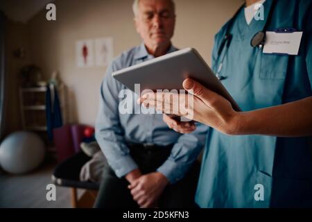 Closeup of female nurse hands holding digital tablet with senior patient sitting in clinic Stock Photo
