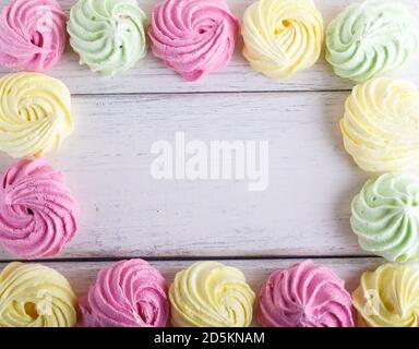 Colorful frame of multicolored meringues on white wooden background. copy space, top view, flat lay. Stock Photo