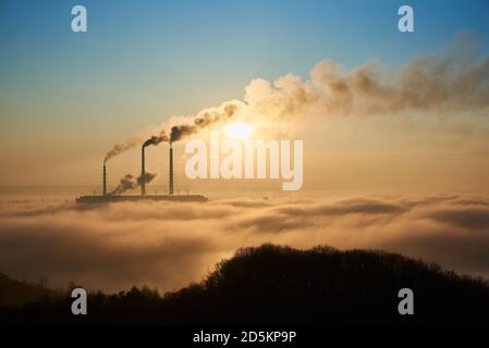 Horizontal snapshot of industrial area at setting sun, three smoking pipes from thermal power station pollute the atmosphere with black smog, concept of man-made disaster and energy generation Stock Photo