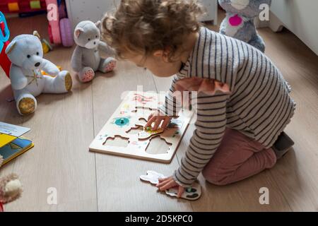 17-month child playing with a wooden jigsaw puzzle, fitting shapes of animals Stock Photo