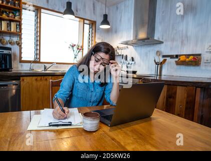 Stressed business woman working from home on laptop looking worried, tired and overwhelmed. Exhausted female working remotely during social distancing Stock Photo