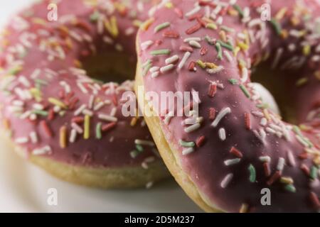 Pink donuts decorated with colorful sprinkles on a white plate . Close up Stock Photo