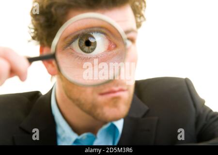 Young man in a suit looks through a magnifying glass Stock Photo
