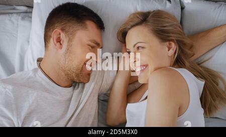 Happy Young Couple Cuddling Together in the Bed, Young Woman is Pregnant and Loving Partner Touches and Caresses Her Tenderly. Top View Shot. Stock Photo