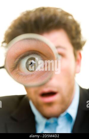 Young man in a suit looks astonished through a magnifying glass Stock Photo