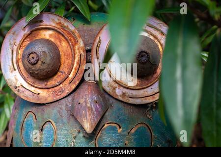 Metal worn owl sculpture outdoors hiding in the bushes. Outdoor sculpture art rusty metal worn. Stock Photo