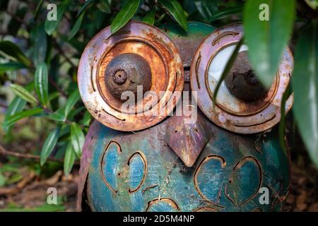 Metal worn owl sculpture outdoors hiding in the bushes. Outdoor sculpture art rusty metal worn. Stock Photo