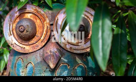 Metal worn owl sculpture outdoors hiding in the bushes. Outdoor sculpture art rusty metal worn. Stock Photo