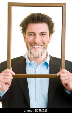 Young man in a suit looks through an empty wooden frame Stock Photo