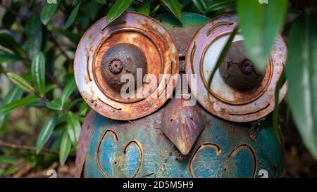 Metal worn owl sculpture outdoors hiding in the bushes. Outdoor sculpture art rusty metal worn. Stock Photo