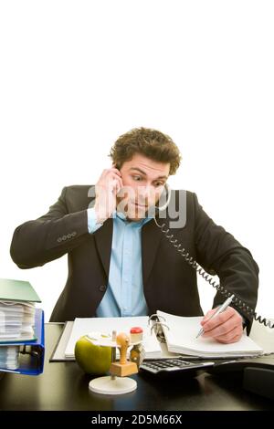 Young man talking on two phones at the same time at his desk and taking notes Stock Photo