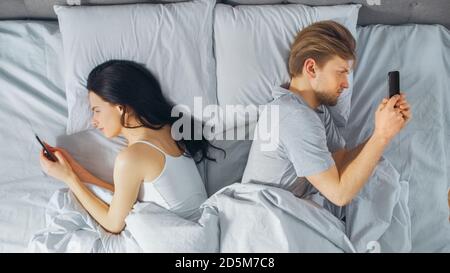 Alienated Millennial Young Couple in the Bed, Young People Turn Away From Each other Using Smartphones, Browsing Through Social Networks and Not Stock Photo