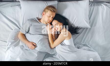 Cute Young Couple Sweetly Sleeping in the Bed, Tenderly Cuddling and Emracing Each other while Dreaming. Early Morning Sun Shines Through the Window. Stock Photo