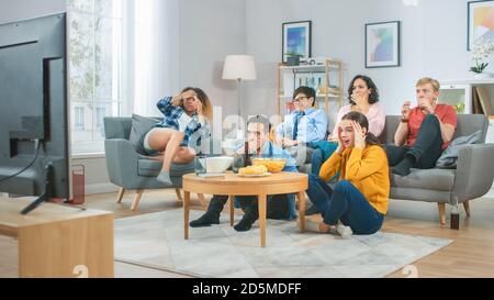 At Home Diverse Group Friends Watching TV Together, Getting Emotionally Terrified and Horrified by the Content of the TV. Young People Are Scared Stock Photo