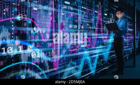 Shot of Asian IT Specialist Using Laptop in Data Center Full of Rack Servers. Concept of Massive Computer Calculations with Visualization Projection Stock Photo
