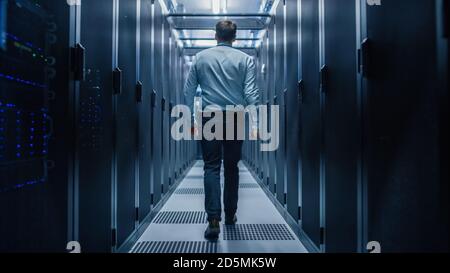 IT Engineer Walking Through Data Center with Working Server Rack to Do Routine Maintenance Check with Laptop. Concept of Cloud Computing, Artificial Stock Photo