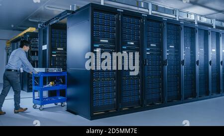 In the Modern Data Center: Team of IT Technicians Working with Server Racks, Running Maintenance and Diagnostics, Checking Networking and Cloud Stock Photo