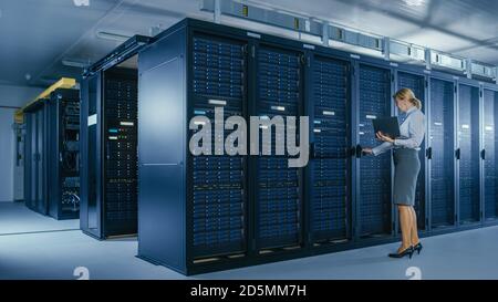In Data Center: Female IT Technician Opens Rack Cabinet and Runs Maintenance Program on Laptop, Controls Operational Server's Optimal Functioning. Stock Photo