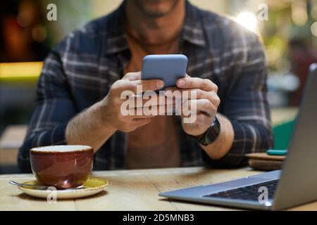 Close-up of man sitting at the table and typing a message on his mobile phone while drinking coffee at cafe Stock Photo