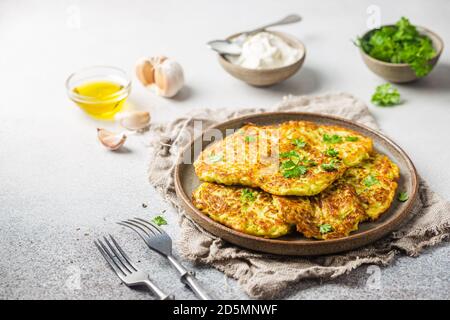 Green zucchini fritters, vegetarian zucchini pancakes with fresh herbs and garlic, served with cream sauce on white background, selective focus Stock Photo