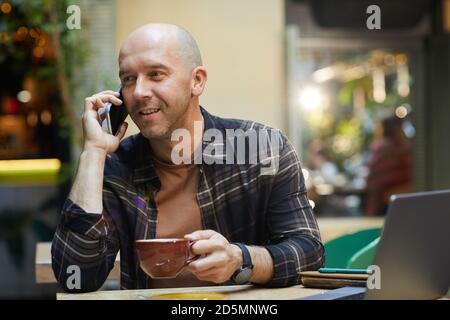 Mature man drinking coffee and talking on mobile phone while working at cafe Stock Photo