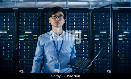 In the Modern Data Center: Portrait of IT Engineer Stand Near Server Racks, Finishing Maintenance and Diagnostics Procedure Holding Laptop. Stock Photo