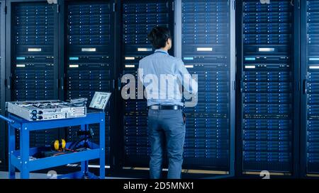In the Modern Data Center: IT Engineer Doing Maintenance and Diagnostics. Works with Opened Cabinet and Installs New Hardware for Planned System Stock Photo