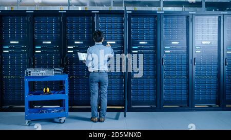 In the Modern Data Center: IT Engineer Doing Maintenance and Diagnostics. Works with Opened Cabinet and Installs New Hardware for Planned System Stock Photo