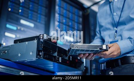 In the Modern Data Center: IT Engineer is Holding New HDD Hard Drive Prepared for Installing Hardware Equipment into Server Rack. IT Specialist Doing Stock Photo