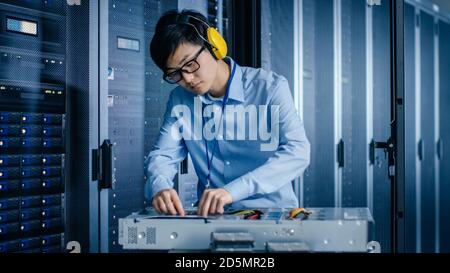In the Modern Data Center: IT Engineer Wearing Protective Muffs Installs New Hardware for Server Rack. IT Specialist Doing Maintenance, Running Stock Photo