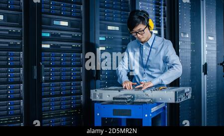 In the Modern Data Center: IT Engineer Wearing Protective Muffs Installs New Hardware for Server Rack. IT Specialist Doing Maintenance, Updating Stock Photo