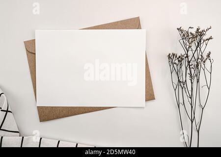 Blank white paper on brown paper envelope with Limonium dry flower and White cloth with Black grid pattern. Mock-up of horizontal blank greeting card. Stock Photo